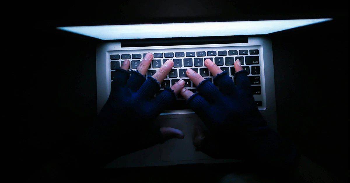 ominous overhead photo of someone wearing fingerless black gloves and typing on a laptop (featured image for an article about the importance of payroll security)