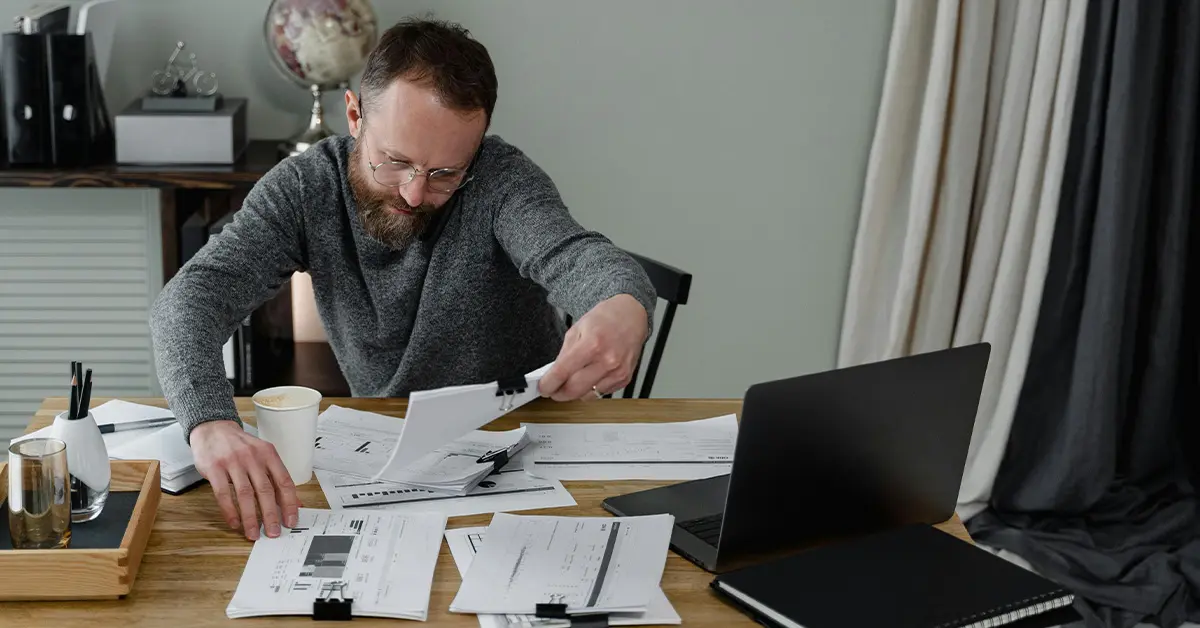 photo of a man sitting at a desk covered with stacks of papers held with binder clips (featured image: "What Is Payroll Automation? The Essential Guide for Businesses" article)