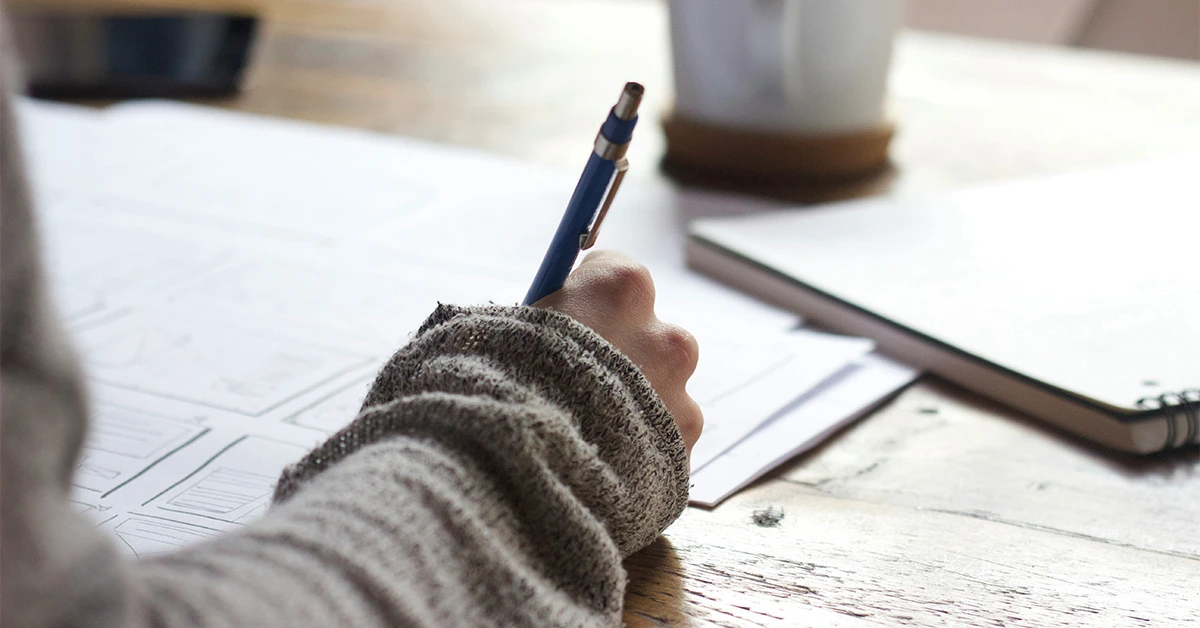 closeup photo of a woman writing at a desk with a notebook resting nearby (featured image: "Onboarding Checklist: Essential Steps for Employee Success" article)